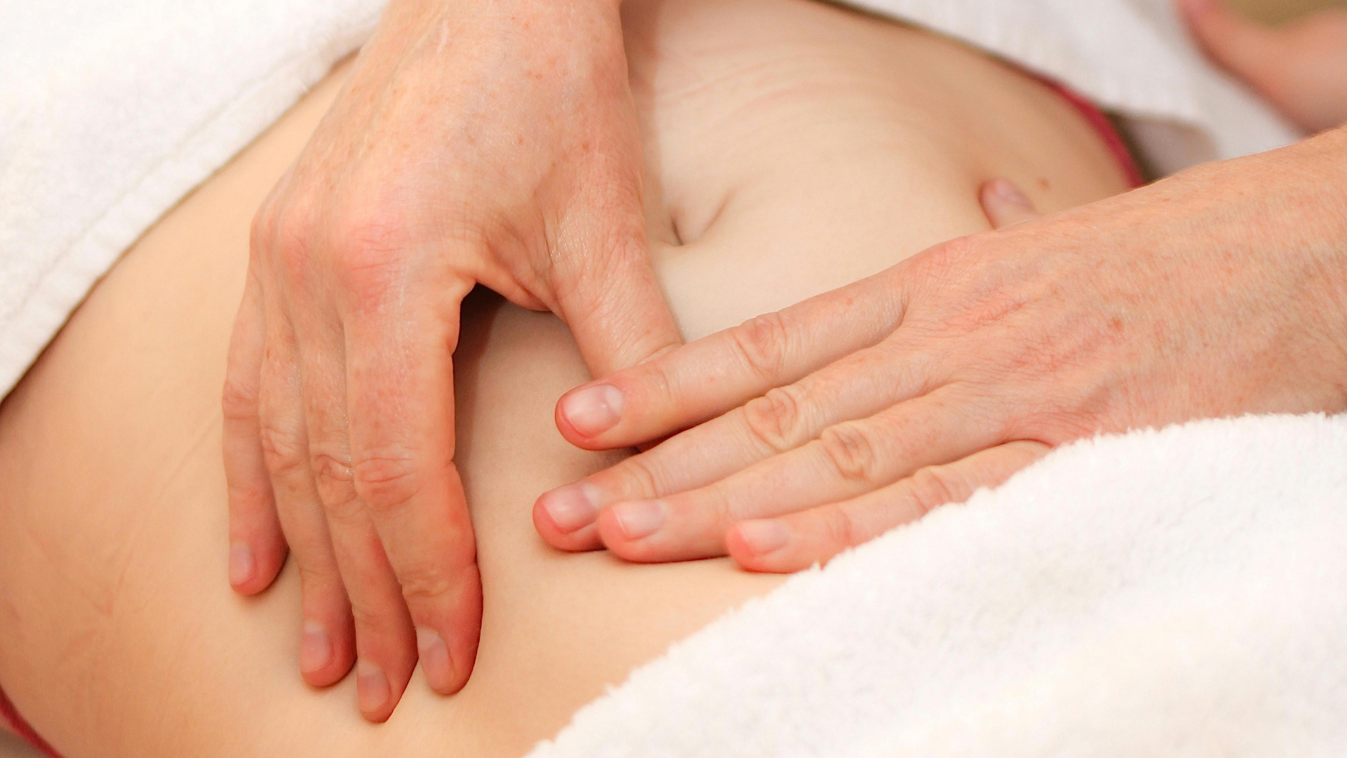 Primeiro plano de uma técnica manual de drenagem linfática abdominal na Jéssica Pereira Fisioterapia. As mãos da profissional aplicam pressão suave e precisa na área abdominal para estimular o sistema linfático e reduzir a retenção de líquidos.