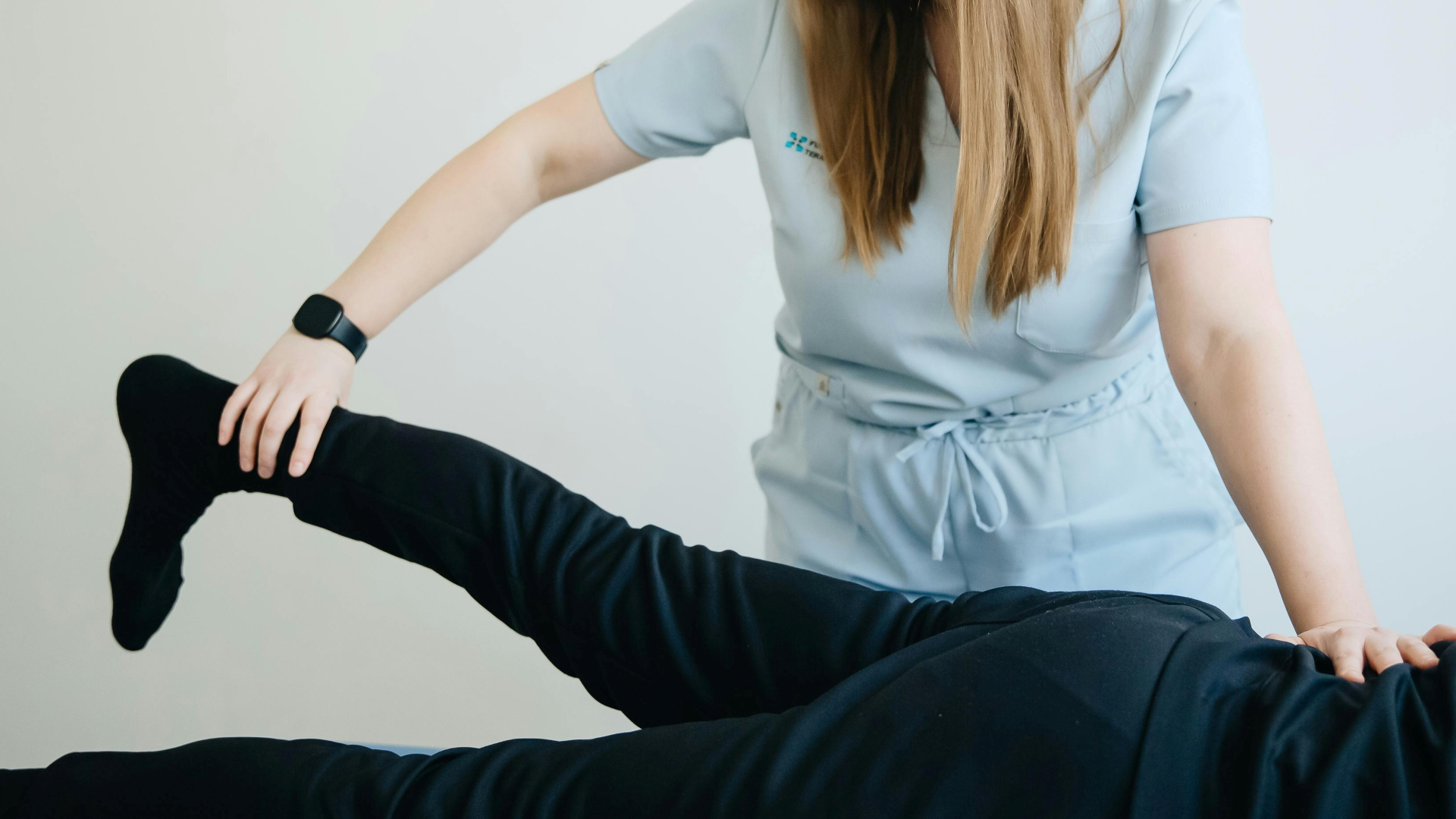 Sessão de reabilitação para fraturas e entorses na Jéssica Pereira Fisioterapia. Uma fisioterapeuta realiza a mobilização assistida da perna e tornozelo de um paciente para recuperar a amplitude de movimento e a força muscular.