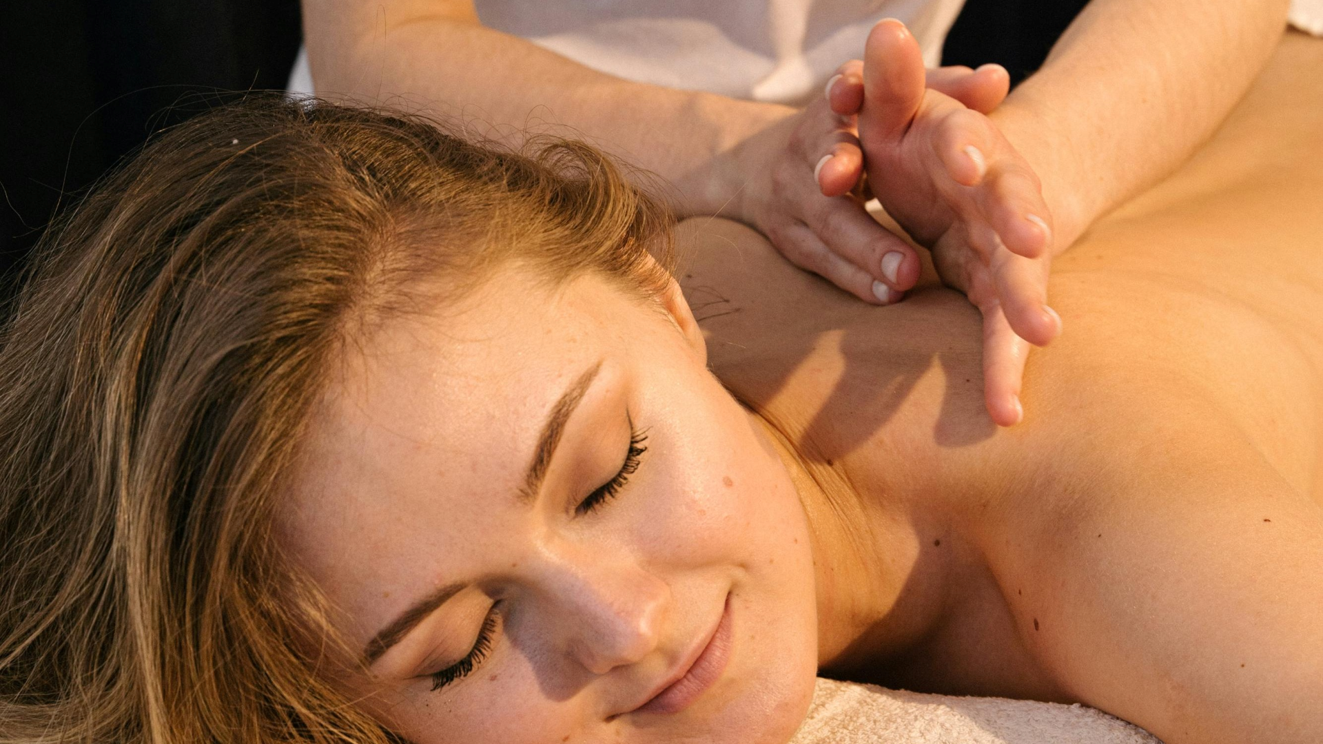Paciente relaxada durante uma massagem de relaxamento na Jéssica Pereira Fisioterapia. A imagem foca no rosto sereno da paciente enquanto a profissional realiza movimentos suaves nos ombros para redução do stress.