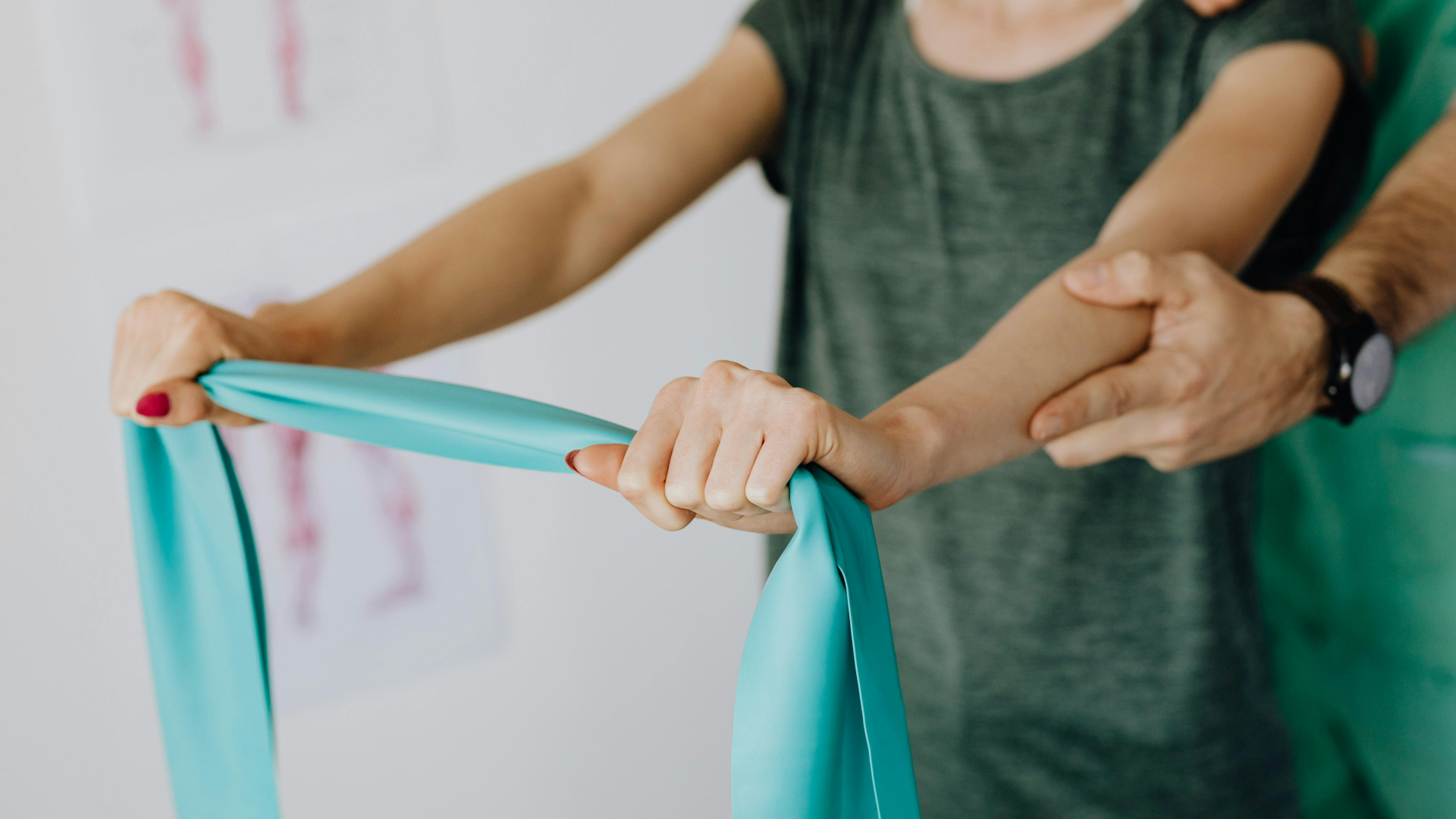 Paciente em exercício de reabilitação pós-cirúrgica na Jéssica Pereira Fisioterapia. A imagem mostra a paciente a utilizar uma banda elástica turquesa para fortalecimento muscular do braço, com o apoio e correção postural de um fisioterapeuta.